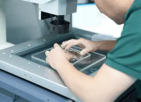 Technician carefully positioning custom glass on a 2D vision measuring system for high-precision dimensional inspection
