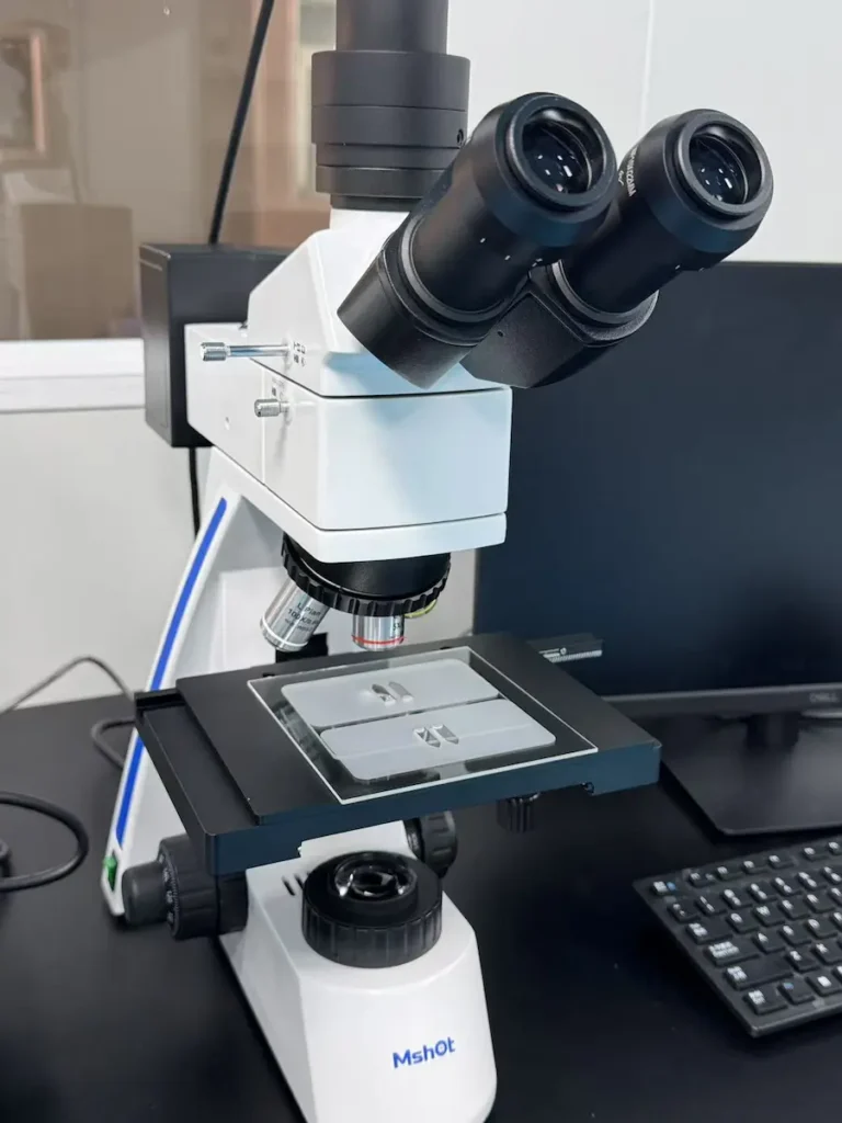 High-magnification optical microscope used for inspecting micro-defects and coating quality on custom glass surfaces

