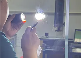 Quality inspector using focused illumination to check for internal defects, bubbles, and impurities in a clear custom glass panel
